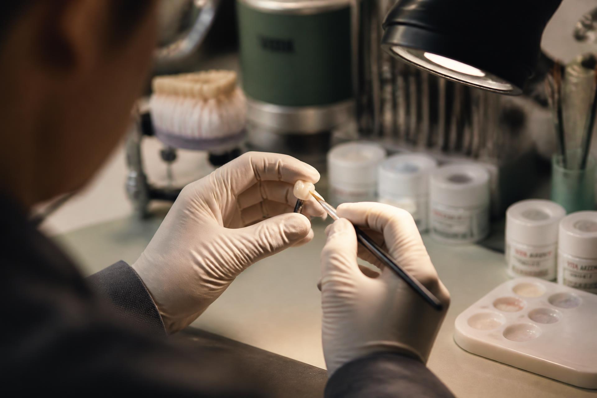 Dental technician hand-glazing a ceramic crown under a task lamp